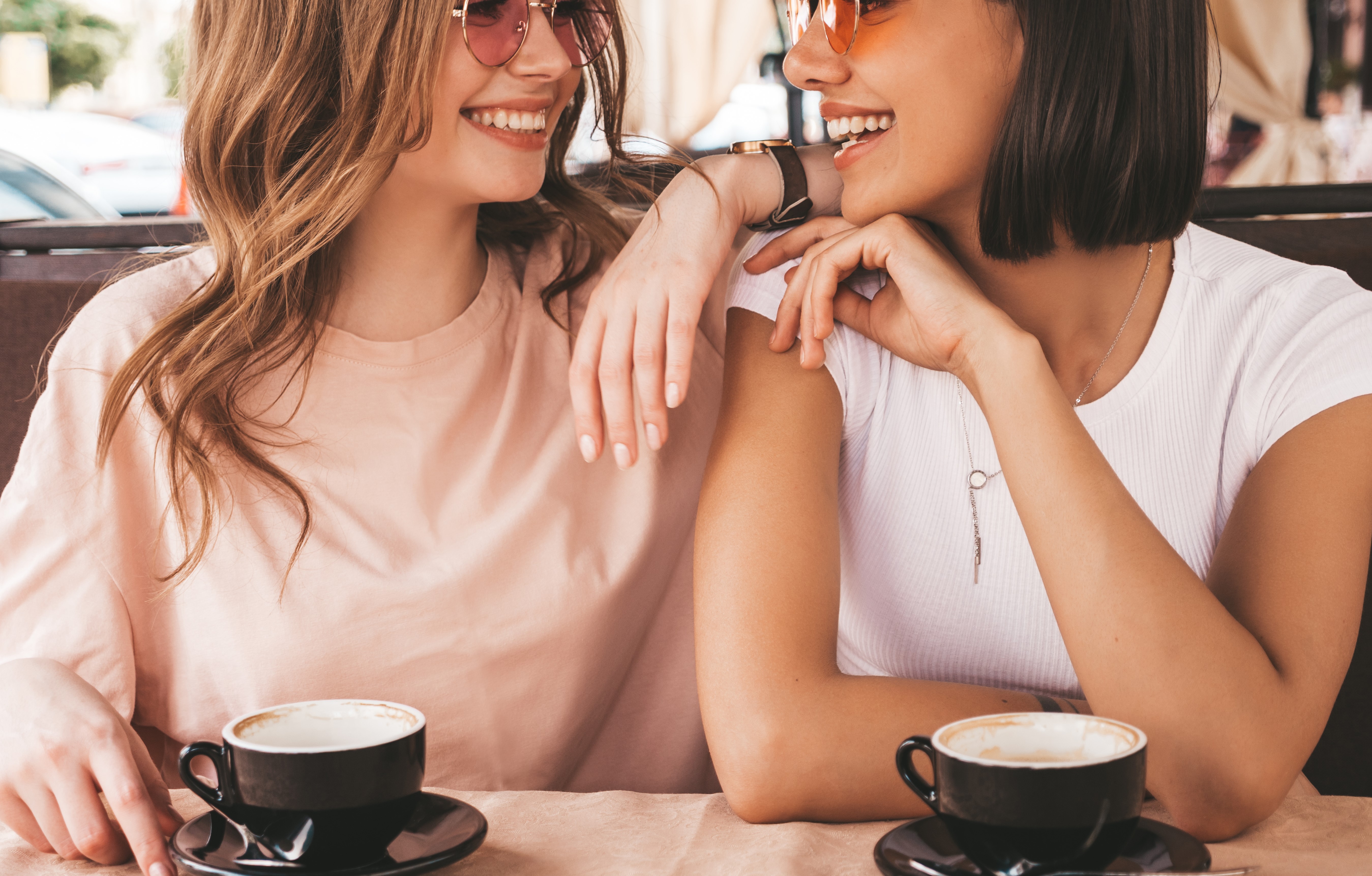 Twee jonge mooie lachende hipster meisjes in trendy zomerkleding zorgeloze vrouwen chatten in veranda terras cafe en koffie drinken positieve modellen met plezier en communiceren